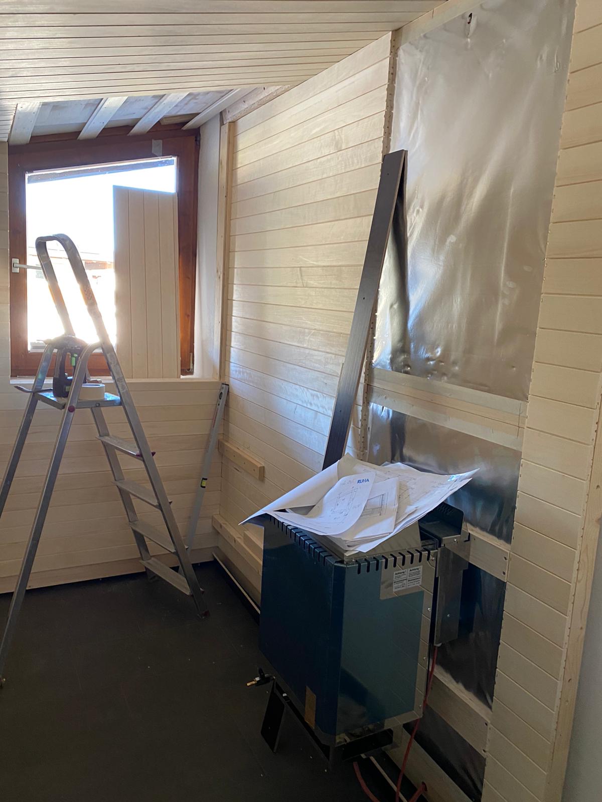 Umbauphase einer privaten Sauna mit Holzverkleidung, Ofen und Planunterlagen
